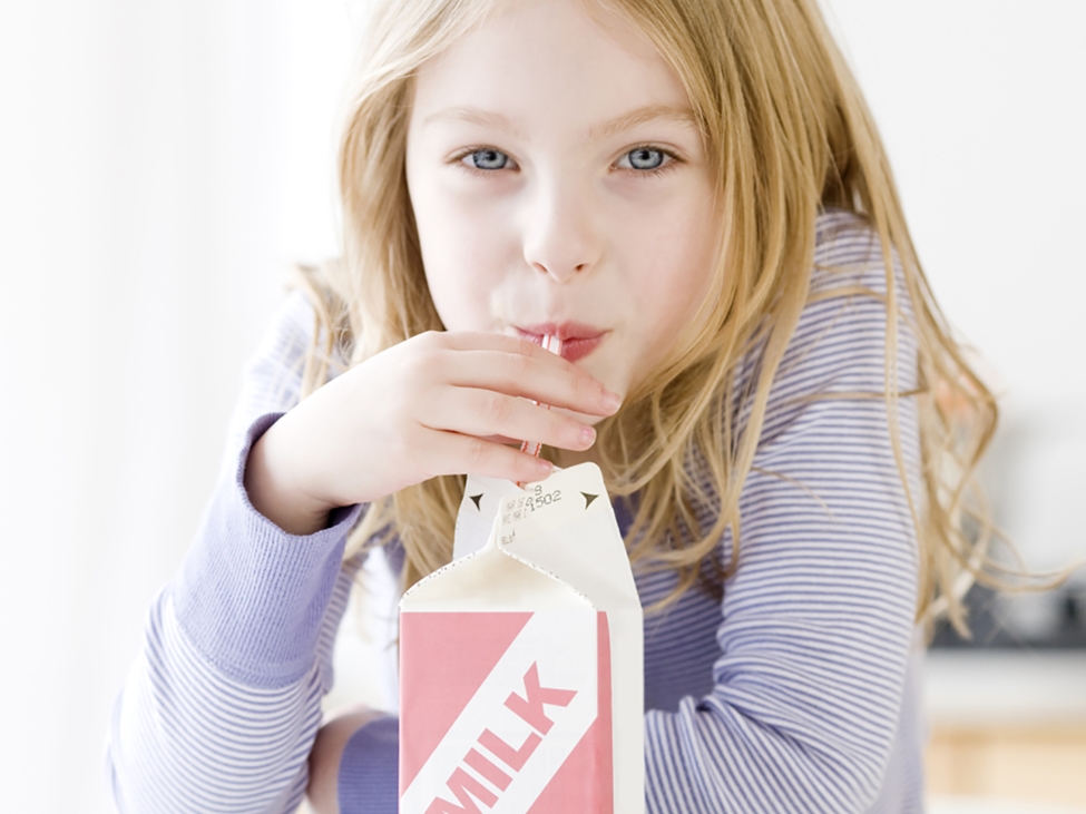 从纸板牛奶容器的女孩喝牛奶。Levasil胶体二氧化硅用于增强纸板股票的摩擦和印刷性能。